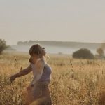 A woman enjoys a serene moment in a sunlit grass field during sunset.