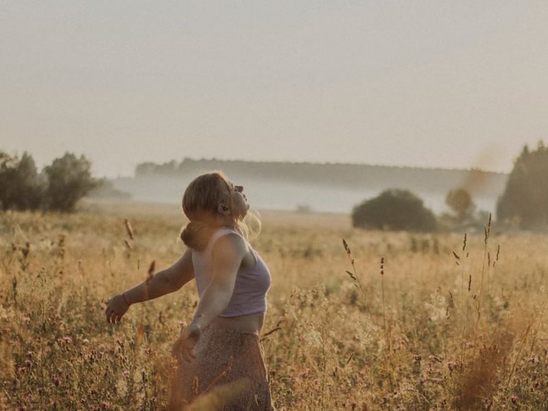 A woman enjoys a serene moment in a sunlit grass field during sunset.