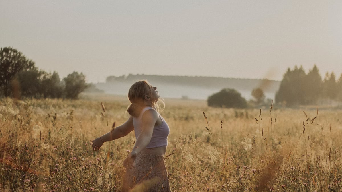A woman enjoys a serene moment in a sunlit grass field during sunset.